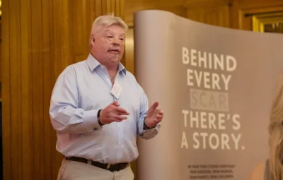 Simon Weston giving a talk in a meeting room with a presentation banner thats reads Behind Every Scar There Is A Story.
