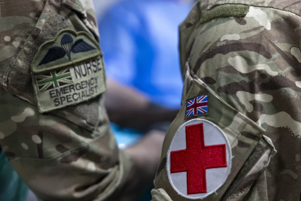 Close-up of British military medical uniforms showing nursing and Red Cross patches on camouflage sleeves.