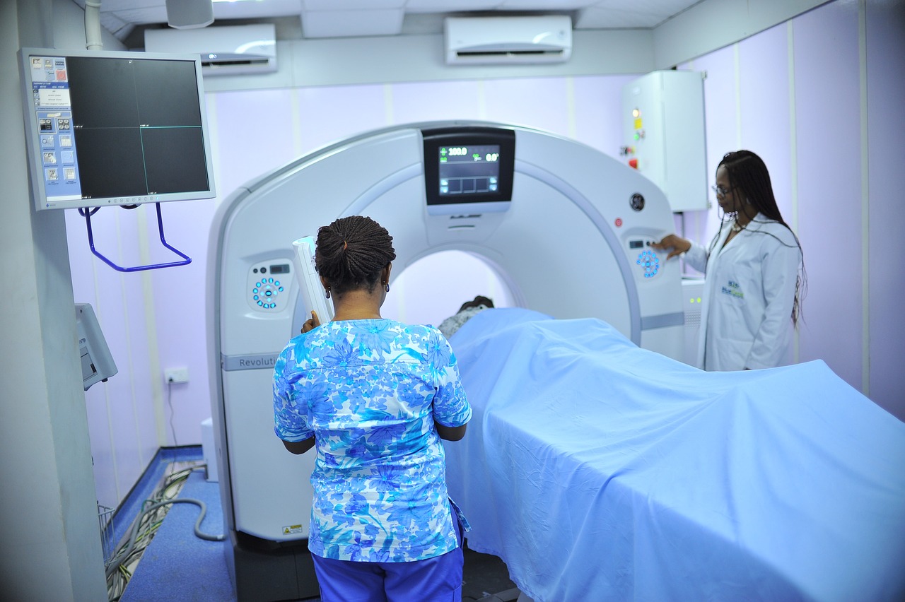 Two medical professionals stand either side of a CT scanner, as a patient lays on the bed about to be scanned.