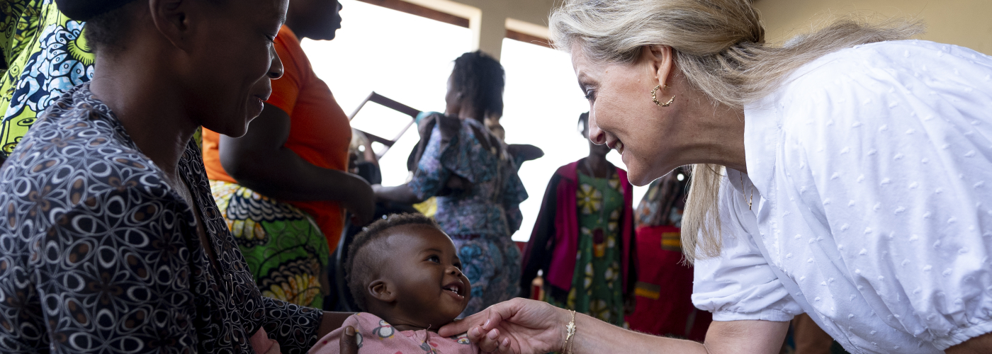 HRH The Duchess of Edinburgh leans down and plays with a baby in its mother's arms