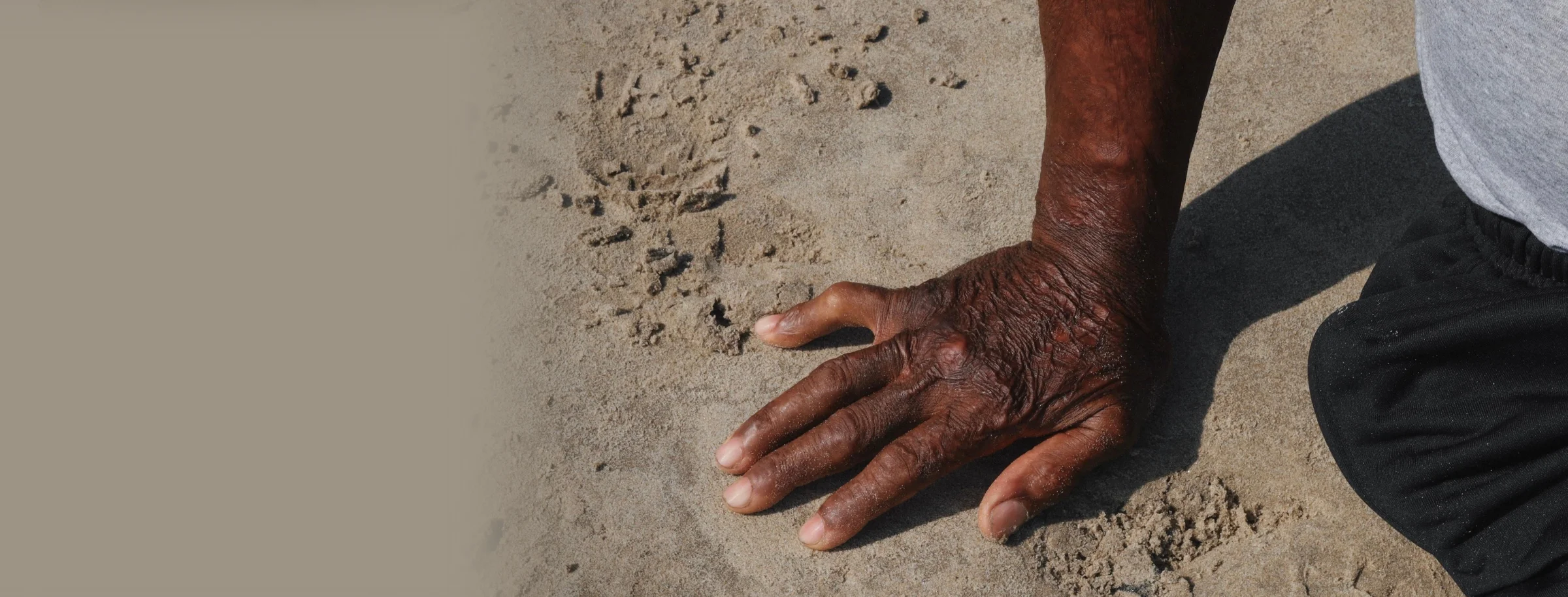 An adult hand touching sand on a beach, showing skin texture and natural lighting.