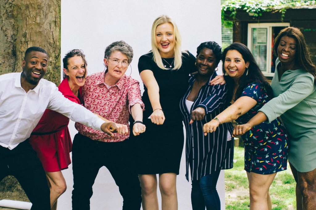 Seven diverse ambassadors posing together outdoors with linked arms, smiling at the camera.