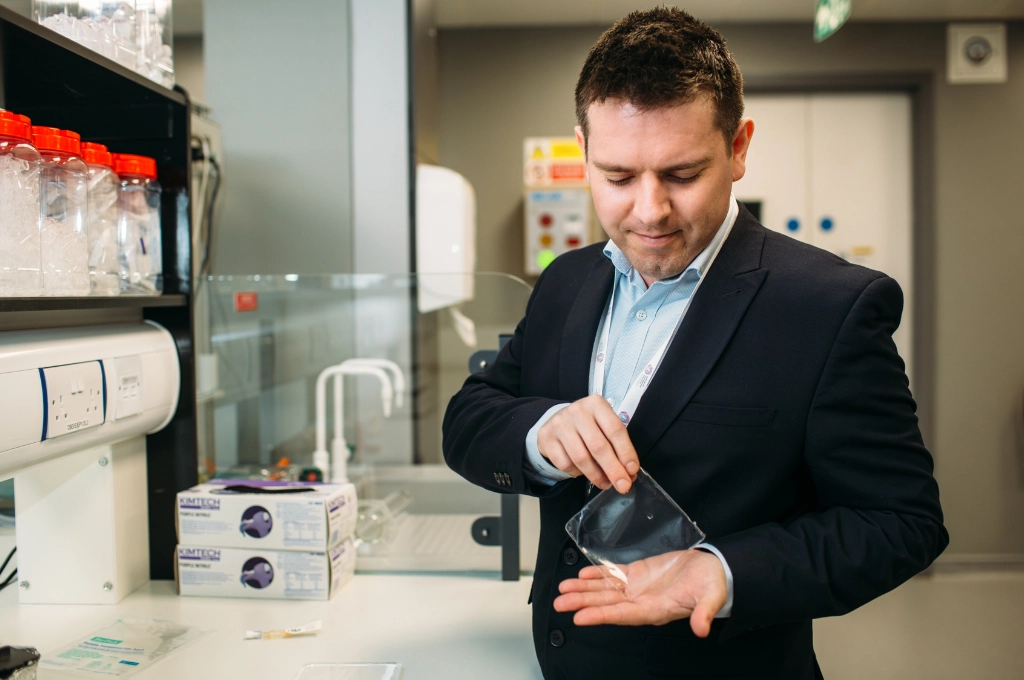 Man in business suit examining a medical sample in a laboratory setting with equipment visible.