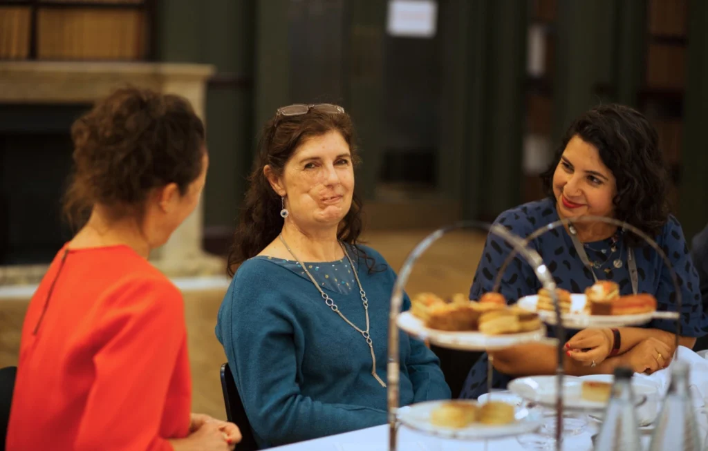 Three women conversing at a formal dinner event with plates of food on the table.