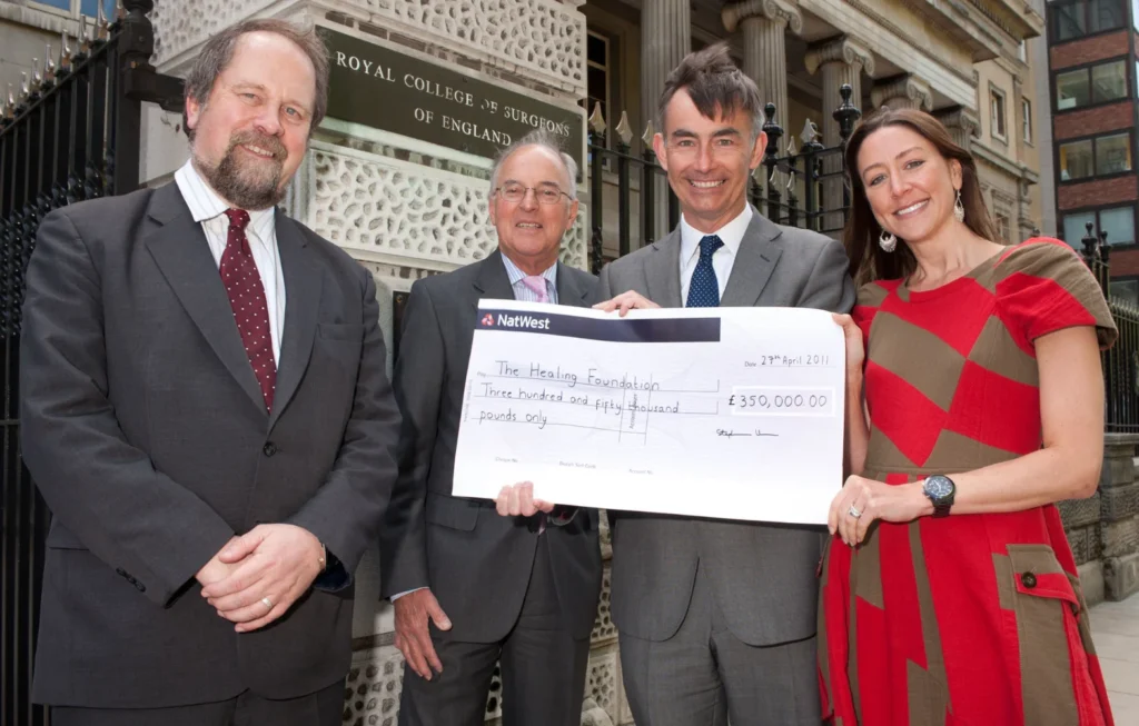 Group of four people in office attire holding a large cheque