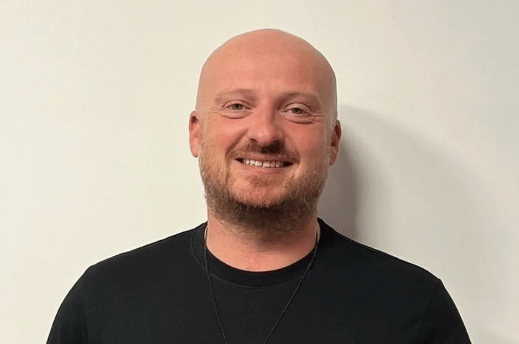 Iwan Roberts smiling at camera, bald man with beard wearing black t-shirt against white background
