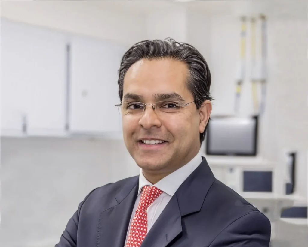 Professional headshot of Liaquat Verjee in business attire with glasses, smiling in an office setting.