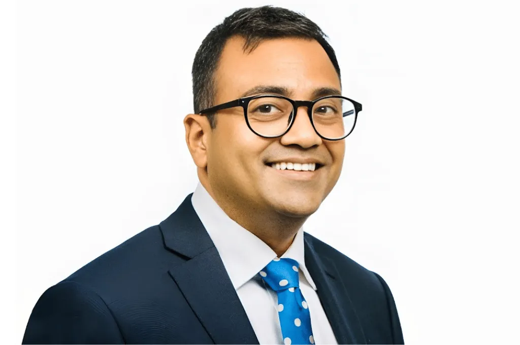 Professional headshot of Sridhar Athreya wearing glasses, dark suit jacket, white shirt, and blue polka dot tie against white background.