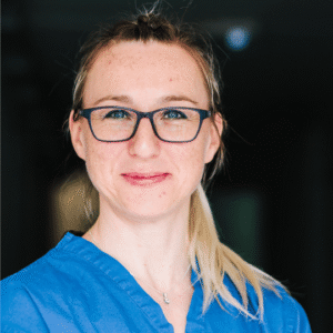 Kristina Stiles, a burns and plastic surgery nurse specialist, and friend of The Scar Free Foundation, wears glasses and blue scrubs and smiles at the camera in this headshot.