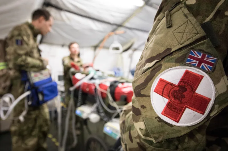 British military medic with Red Cross armband patch on uniform in field medical tent.