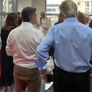 Professor Bruce Keogh, Scar Free Foundation Chairman and former Medical Director of NHS England, holds a microphone as he addresses guests. He wears a cream suit and white shirt in an airy office space.