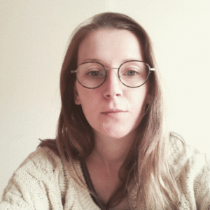 Dr Mary Keeling wears a cream jumper and glasses and sits before a cream background.