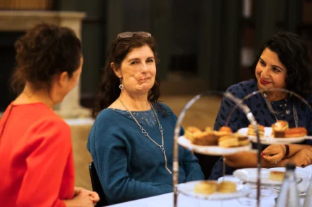 Three women at a social gathering enjoying food and conversation together at a table.