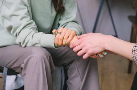 Two hands with green nail polish held together in a gesture of support and comfort.