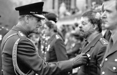 Black and white photo of The Duke of Edinburgh in full uniform pinning a medal on a uniformed Simon Weston on parade.